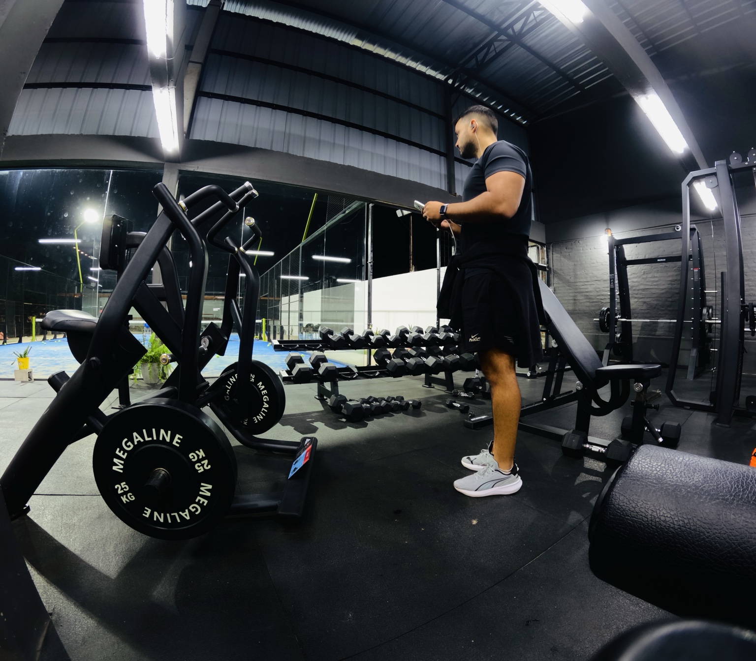 ALEN de perfil en un gimnasio oscuro, junto a máquinas y mancuernas.